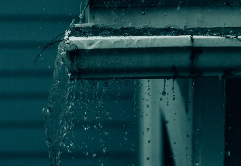 Water pouring over the front edge of a gutter during heavy rain and falling past the downspout.