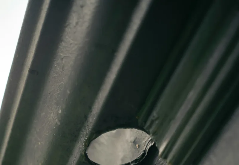 A close view of the outlet hole cut into the bottom of a dark gutter, where the downspout drops away beneath it.
