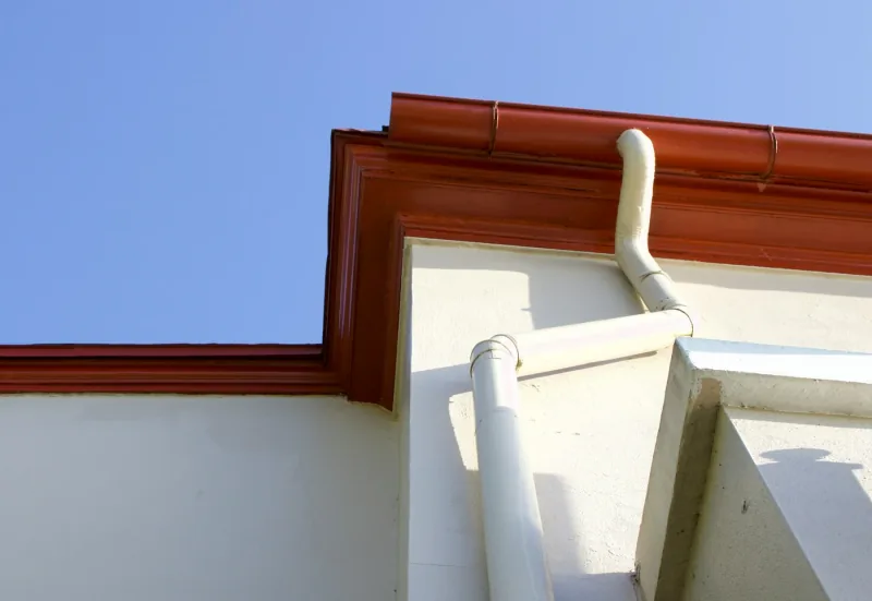 A long unbroken run of gutter along a straight white eaves line against a clear sky, turning down into a downspout at the corner.